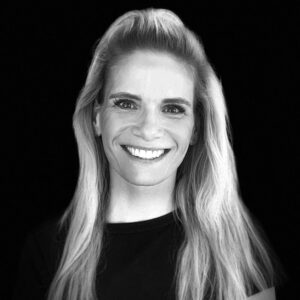 PACE events Schwarz-Weiß-Porträt einer Frau mit langen, hellen Haaren, die lächelt und ein dunkles Oberteil trägt, vor einem soliden schwarzen Hintergrund.