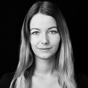 PACE events Schwarz-Weiß-Porträt einer jungen Frau mit langem, glattem Haar und neutralem Gesichtsausdruck, die vor einem schlichten schwarzen Hintergrund direkt in die Kamera schaut.
