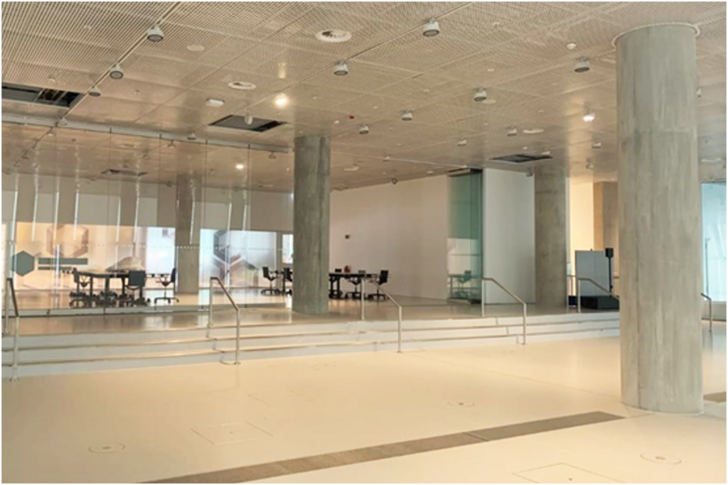 PACE events Ein geräumiger, moderner Innenraum mit hellen Böden und Decken, großen Betonsäulen, Glaswänden und einigen im Hintergrund sichtbaren Besprechungstischen und Stühlen. Der Bereich ist gut beleuchtet und offen gestaltet.