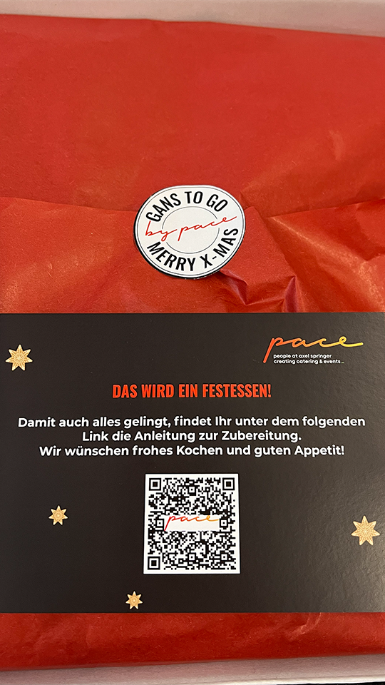 Eine festlich rot verpackte Gans To Go-Verpackung trägt einen Aufkleber mit der Aufschrift MERRY X-MAS. Darunter befindet sich eine Karte in deutscher Sprache mit goldenen Sternen und einem QR-Code, die himmlische Kochanleitungen und herzliche Weihnachtswünsche enthält.