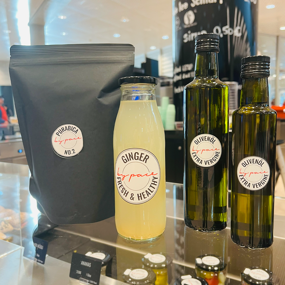 Drei Produkte auf einer Theke: Furrabica No. 2-Kaffee, eine Glasflasche Ingwerdrink - perfekt für die kalte Jahreszeit - und zwei dunkle Flaschen natives Olivenöl extra, alle mit weißen, handgeschriebenen Etiketten, die in jede stilvolle Küche passen.