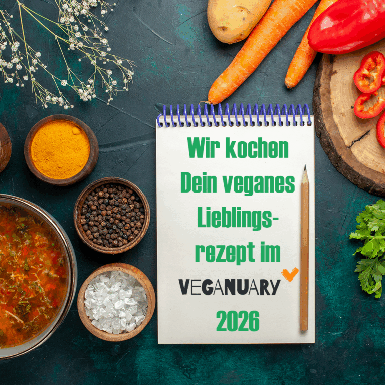 Ein Notizblock mit einem deutschen Text über veganes Lieblingsgericht für Veganuary 2026 liegt auf einem Tisch, umgeben von Gemüse, Gewürzen und einer Schüssel Suppe.