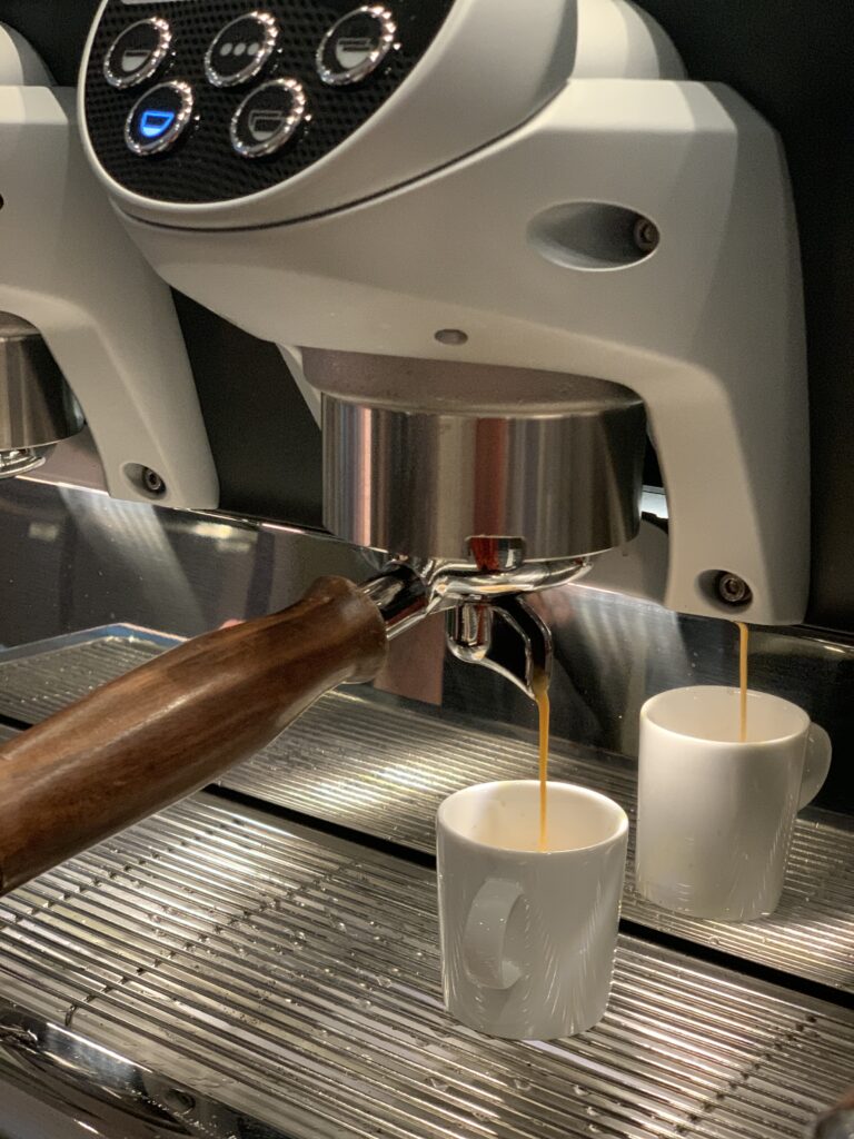 Die Espressomaschine brüht den Kaffee in zwei weiße Tassen, aus deren Siebträger ein satter Strahl auf eine Metallabtropfschale fließt - perfekt, um Kitchen Insights zu sammeln oder bei einer frischen Tasse ein Gespräch zu beginnen.