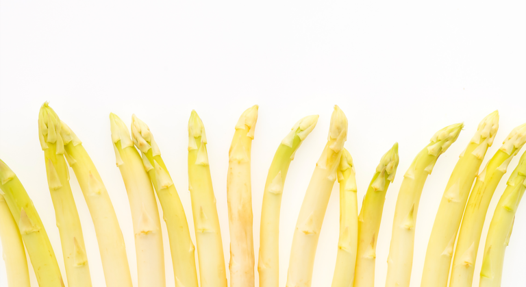 Eine Reihe frischer weißer Spargelspieße steht aufrecht vor weißem Hintergrund, die Spitzen zeigen nach oben - der perfekte Mittelpunkt für jedes Frühlings-Dinner im JOURNALISTENCLUB.