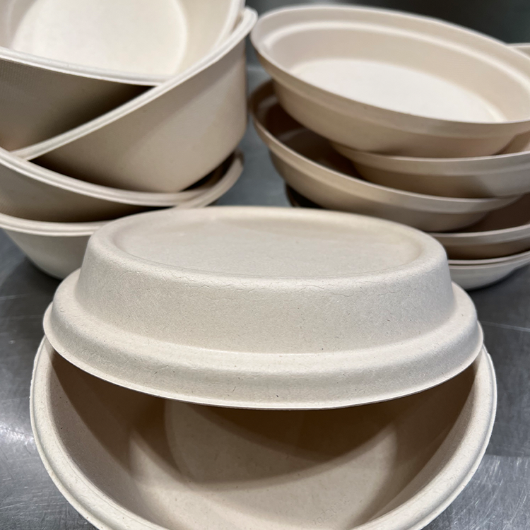 Eine Nahaufnahme mehrerer gestapelter beigefarbener biologisch abbaubarer Schalen und Deckel aus nachhaltigem, kompostierbarem Material, perfekt für Mittagessen oder Kaffee, angeordnet auf einer Metalloberfläche.