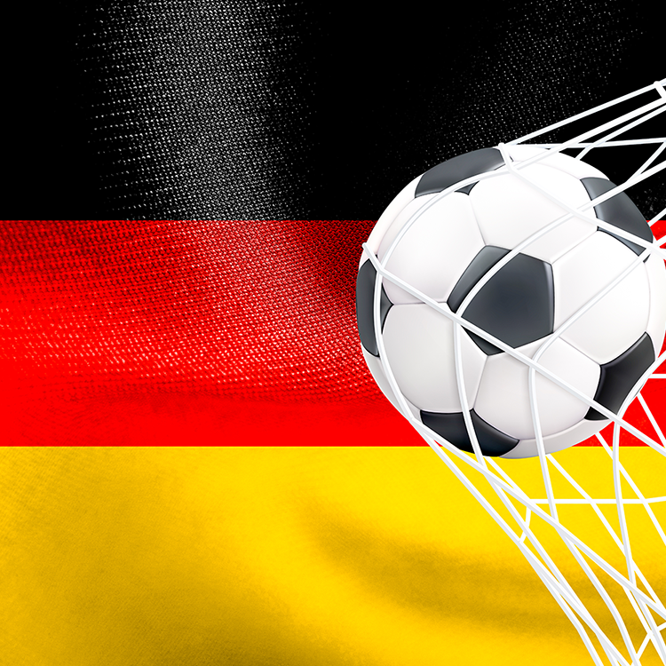 Ein Fußball landet im Netz eines Tores vor einer wehenden deutschen Flagge mit schwarzen, roten und gelben Streifen – „wir können es einfach nicht lassen“ – und verdeutlicht damit die ungebrochene deutsche Leidenschaft für den Fußball.