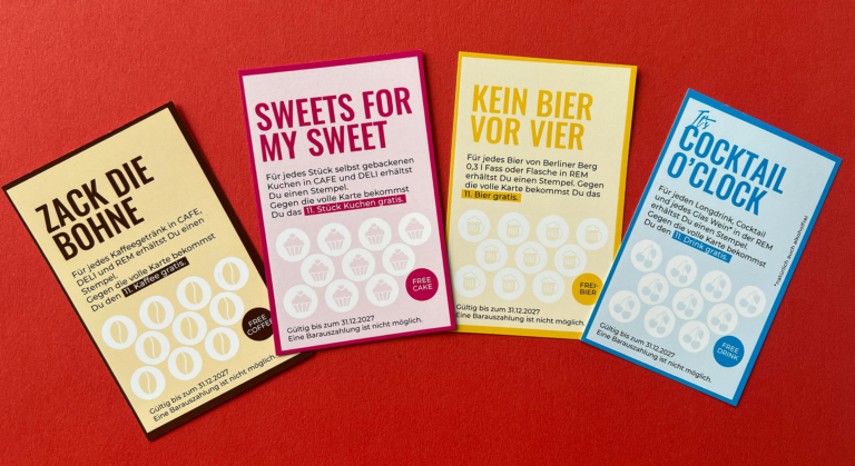 Vier farbenfrohe deutsche Bonuskarten mit verspielten Titeln liegen auf einem roten Untergrund aus. Jede Karte ist mit Kreisen zum Stempelsammeln versehen und bietet Gratisprämien für Kaffee, Süßigkeiten, Bier oder Cocktails, sobald genügend Stempel gesammelt wurden.