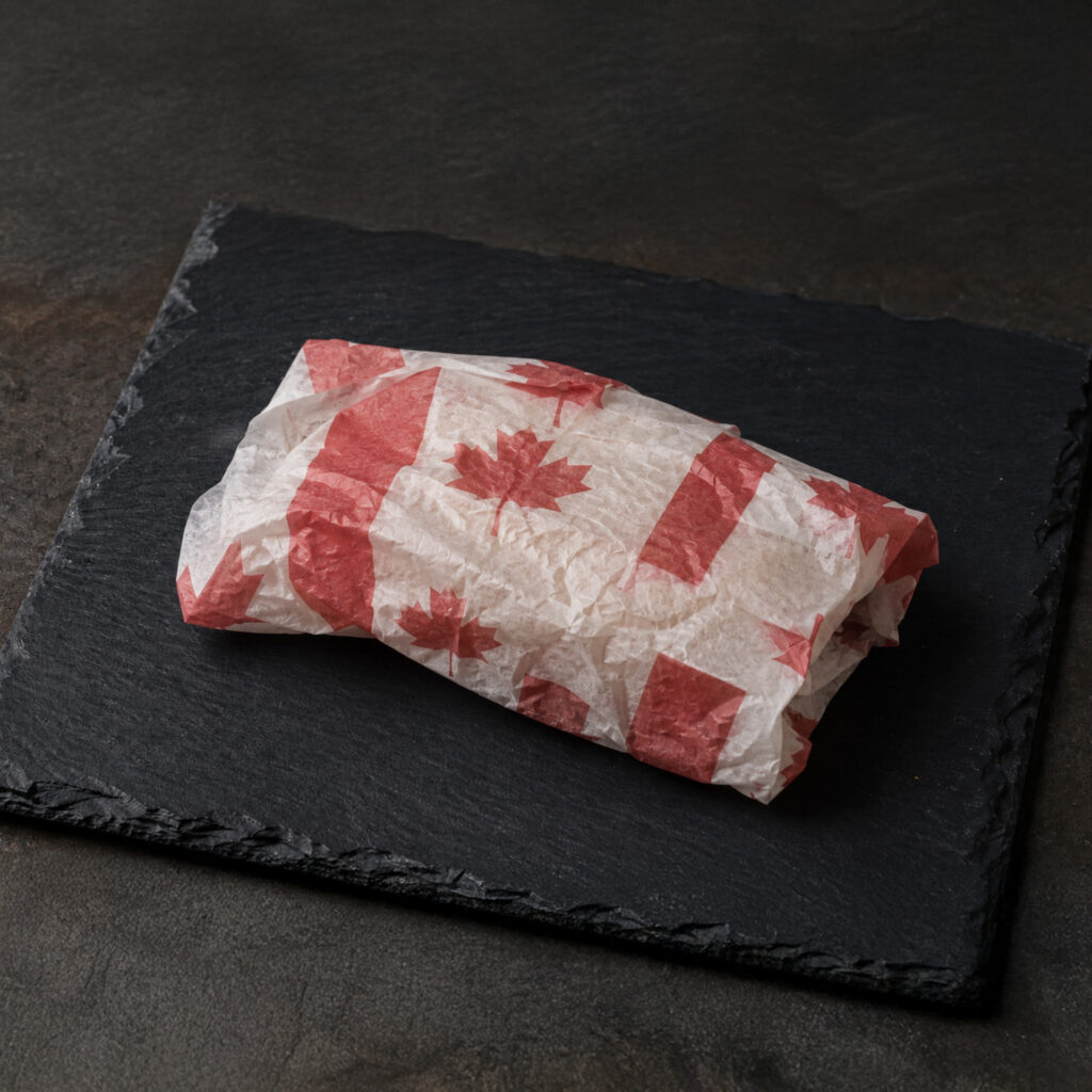 A wrapped object on a dark slate surface, wrapped in paper printed with red maple leaves and Canadian flags, suggesting packaging with a Canadian theme.