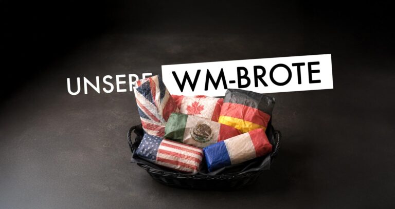 Ein Korb mit Broten, die in Papier eingewickelt sind, das an verschiedene Nationalflaggen erinnert, und über dem der Text UNSERE WM-BROTE steht, lädt zu einer kulinarischen Weltreise mit den speziellen WM-Broten von DELI ein.