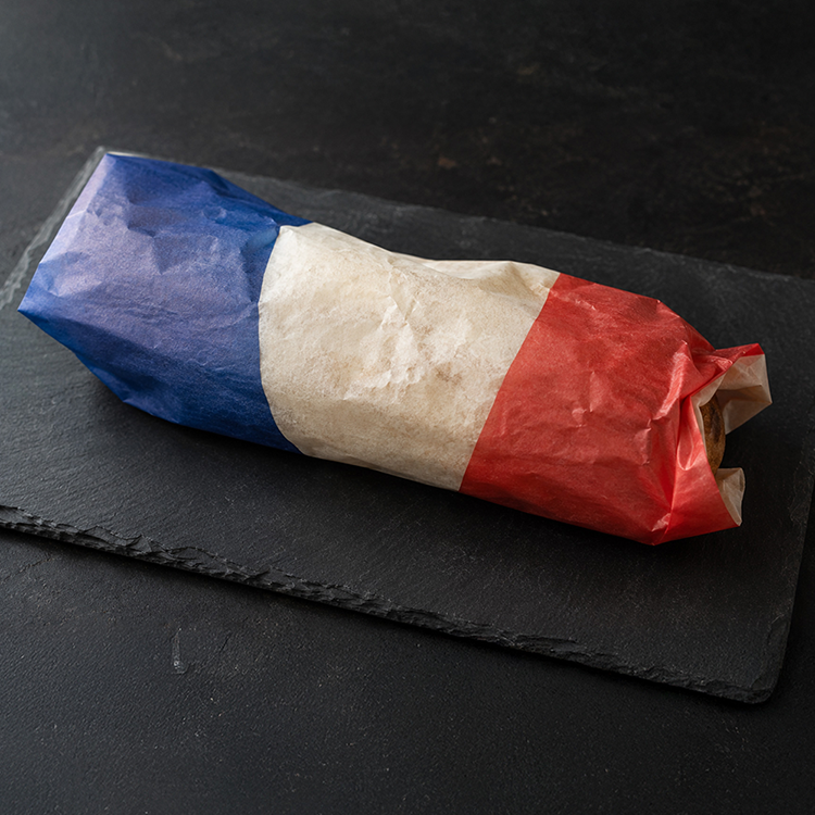 Ein eingewickeltes Sandwich oder ein Burrito auf einer Schieferplatte, umhüllt von Papier mit blauen, weißen und roten Streifen, das an die französische Flagge erinnert.